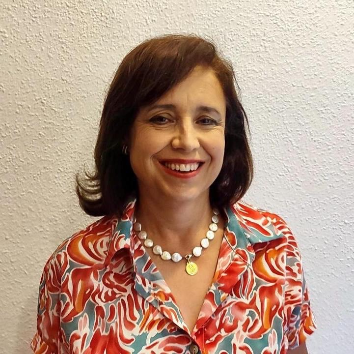 Mujer sonriente con cabello castaño, camisa colorida y collar de perlas, sobre fondo blanco texturizado.