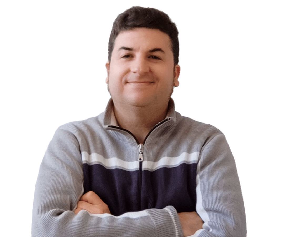 Persona con suéter gris y azul, sonríe con los brazos cruzados sobre fondo blanco.